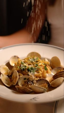 Fresh pasta served with clams in a white bowl, topped with grated cheese and herbs at Sparrow Italia Miami.