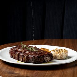 Grilled steak with fresh herbs and roasted garlic on a white plate at Sparrow Italia Miami.