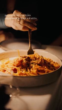 Fresh pasta dish served in a white bowl with a hand holding a fork, highlighting rich Italian cuisine.