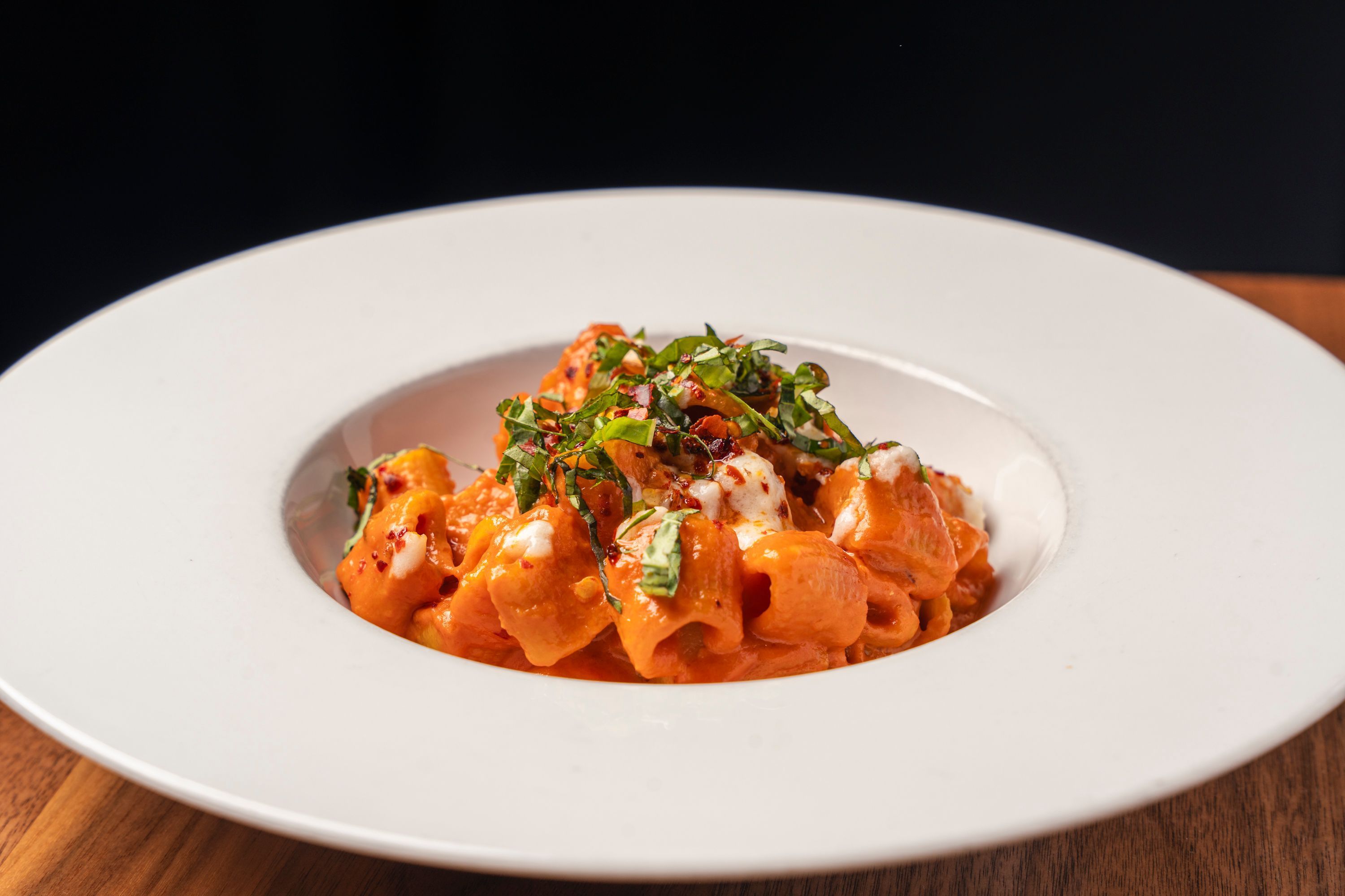 Fresh pasta served with creamy red sauce and garnished with chopped basil on a white plate at Sparrow Italia Miami.
