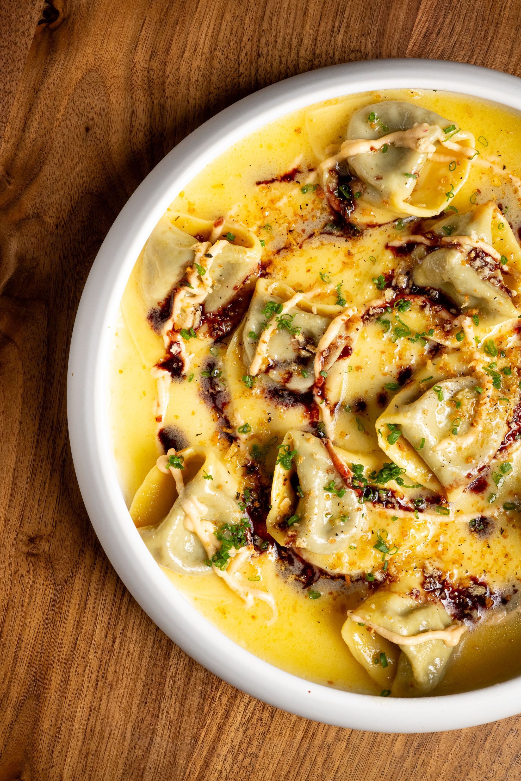 Italian fresh pasta served in creamy yellow sauce garnished with herbs and drizzled with dark balsamic glaze.