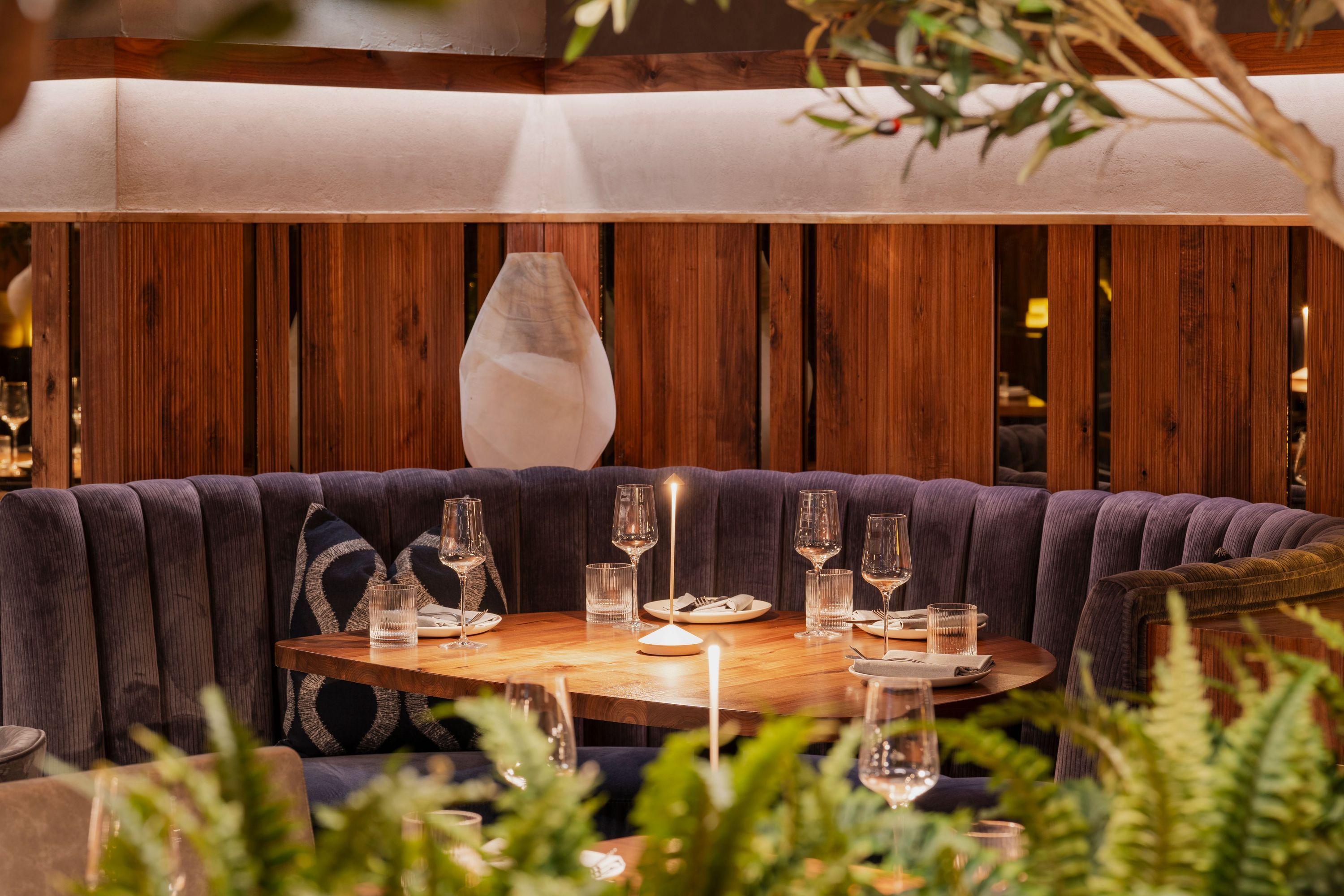 Cozy corner seating with a round wooden table, candles, glassware, and purple cushioned bench at Sparrow Italia Miami.
